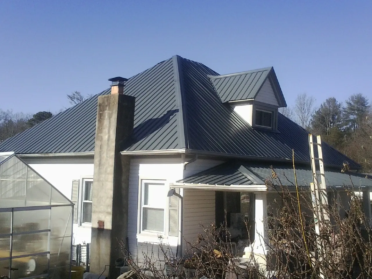 Dark blue standing seam metal roof on a white farmhouse with dormer — Slate & Tile Roof Repair by Roofing Brothers in Leonard
