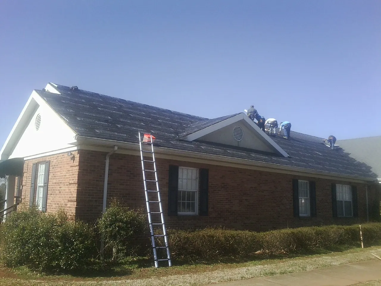 Crew tearing shingles off a brick ranch roof with a ladder set — Metal Roof Repair work by our crew in Leonard