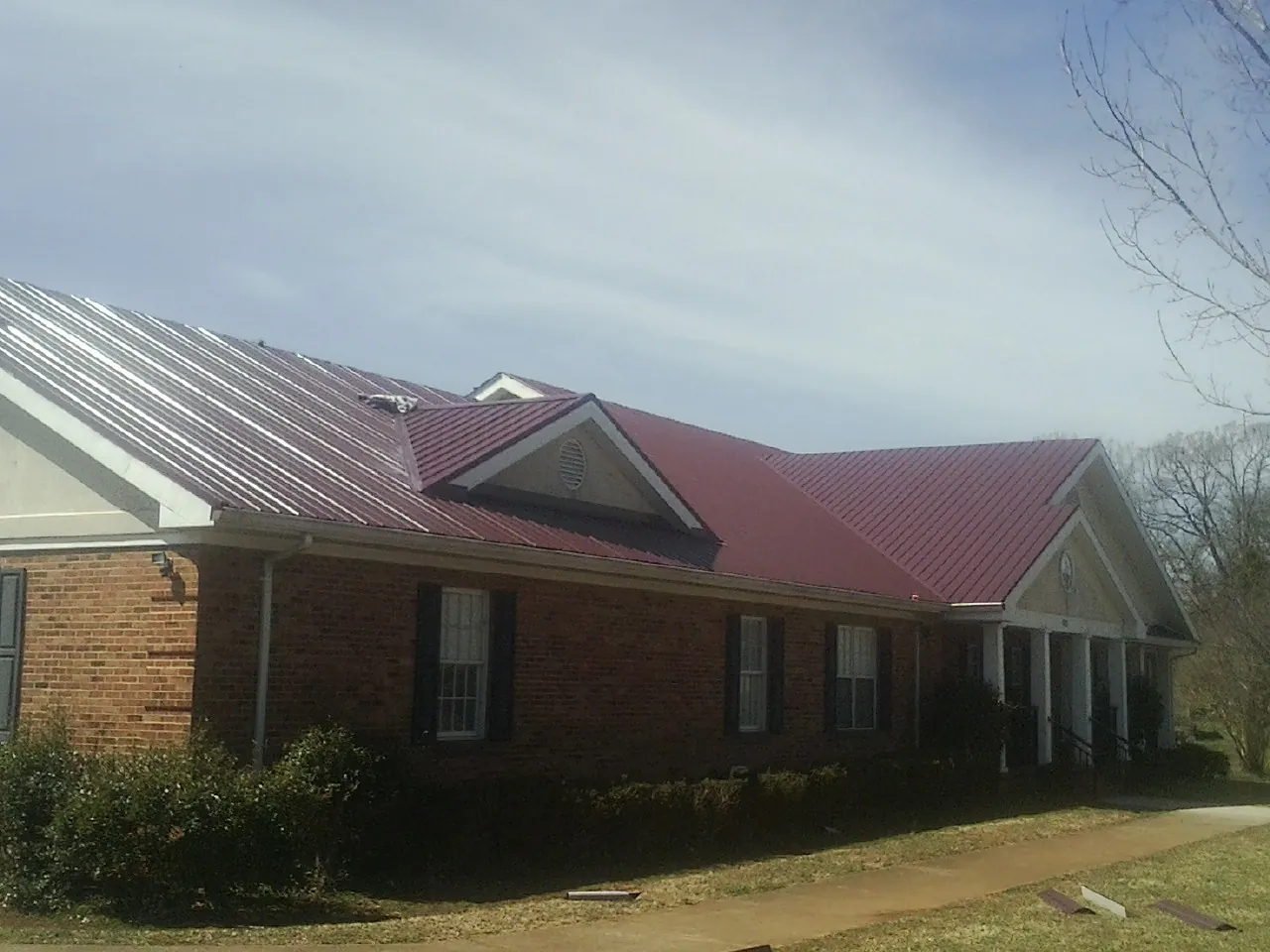 Red metal roof with gabled entries on a long brick building, from a Hail Damage Roof Repair job in Leonard