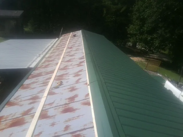 Old rusted panels beside newly installed green metal roofing — Wind Damage Roof Repair by Roofing Brothers in Leonard