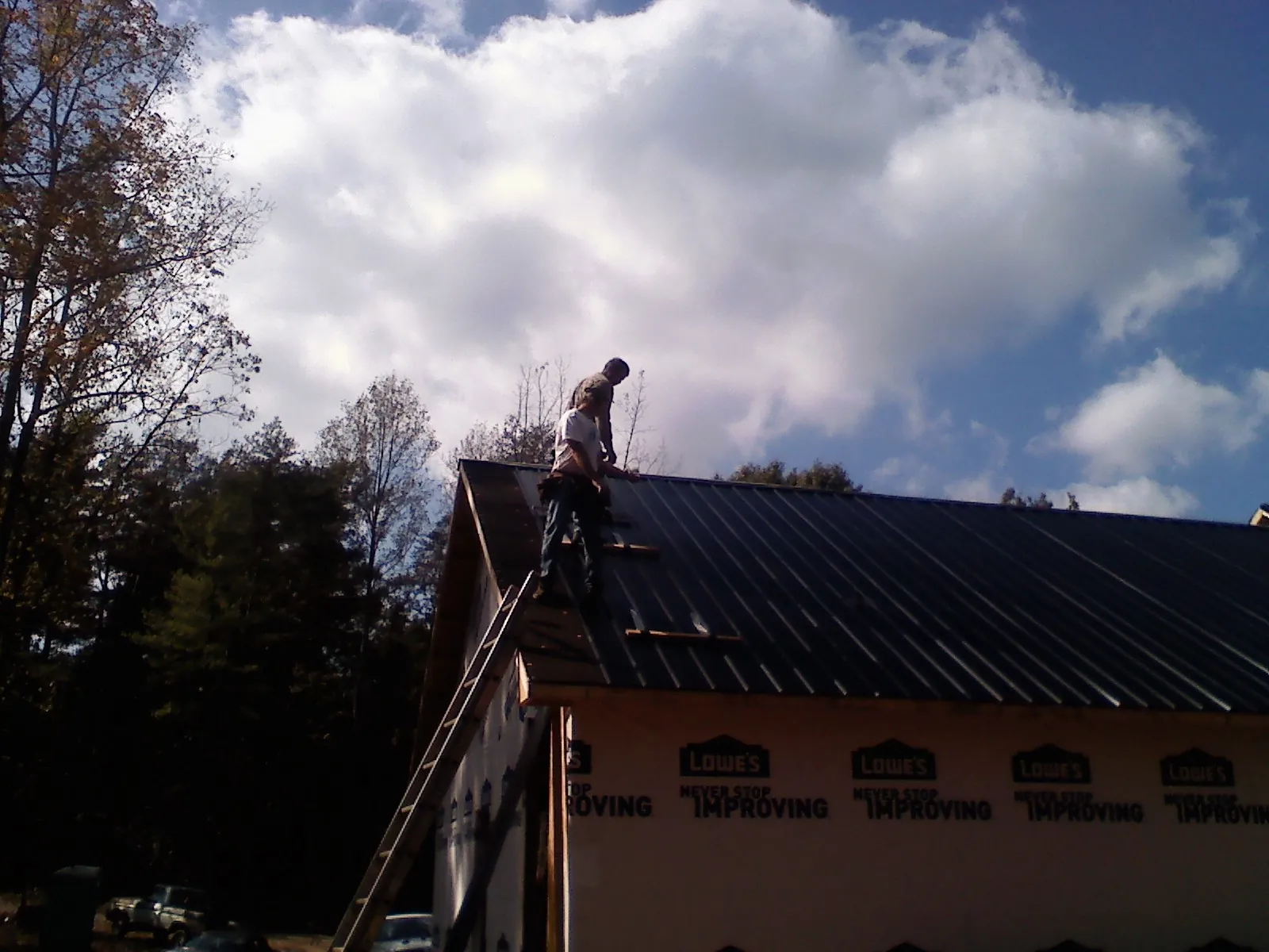 Roofer fastening dark metal panels high against a cloudy sky, from a Roof Inspection job in Leonard