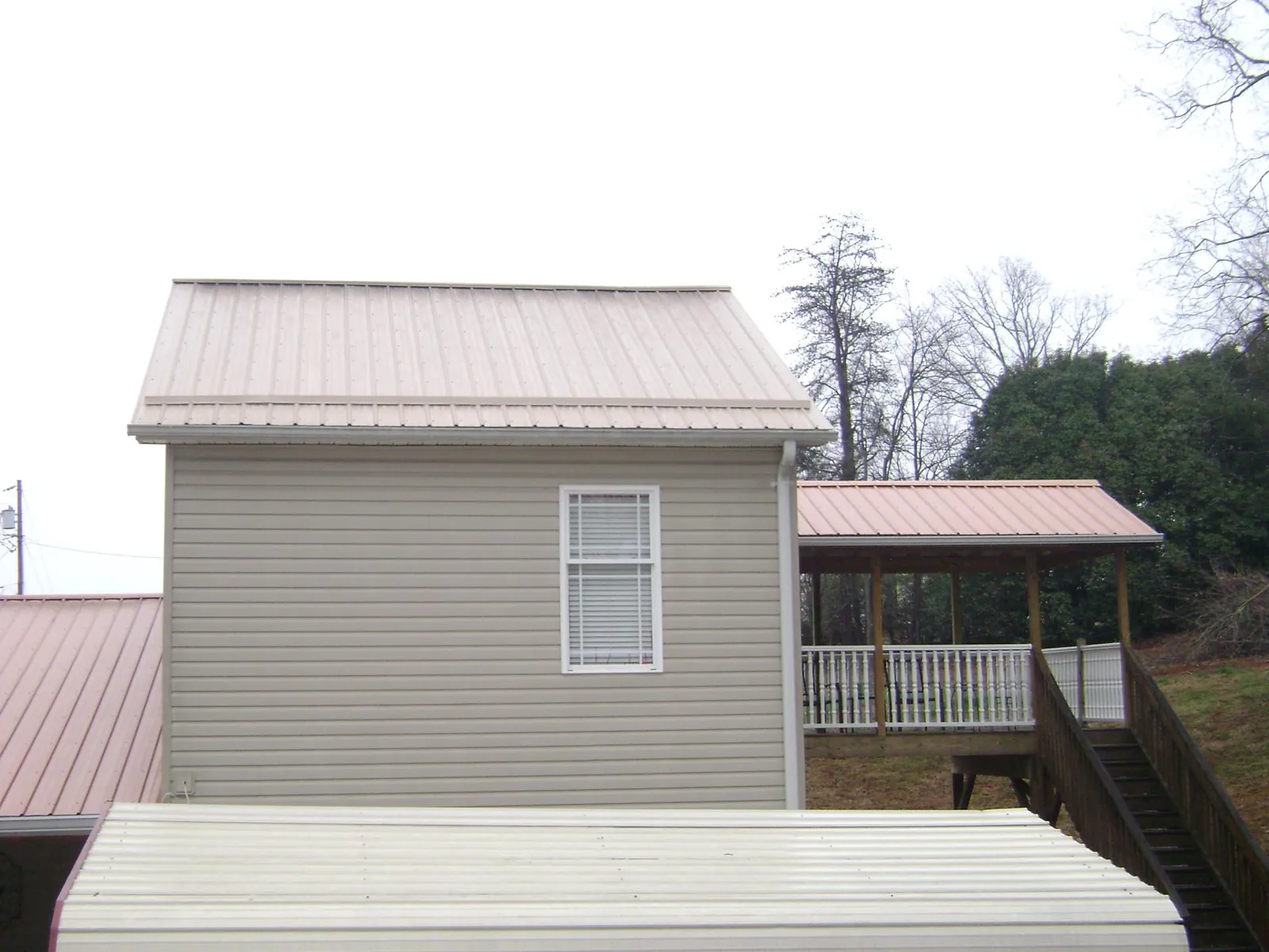 Tan metal roofs on a two story addition and attached porch, from a Roof Replacement job in Leonard